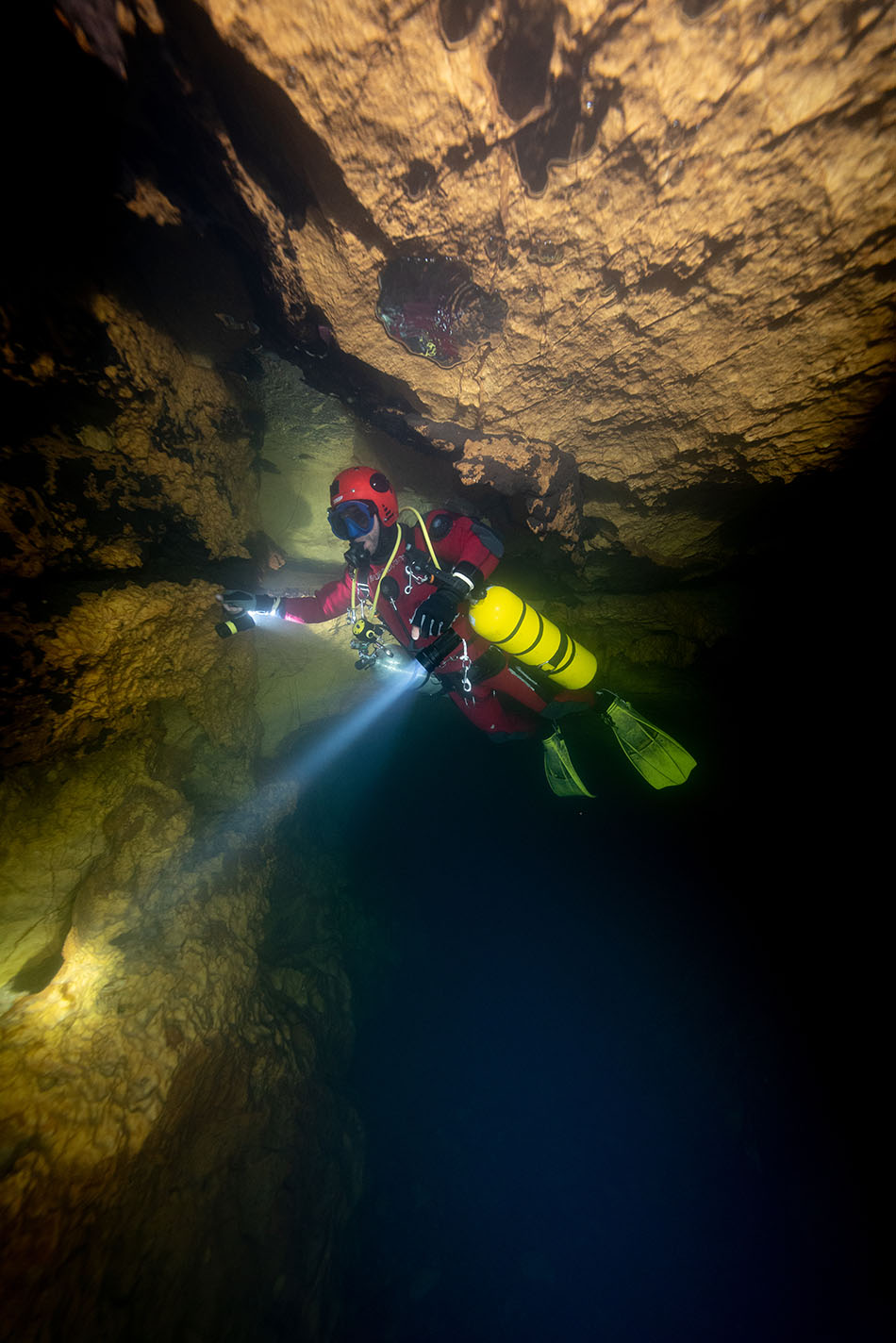 Exploratory diving in an underwater cave, illuminated by a lamp, revealing rock formations.