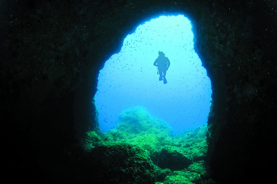 Underwater diving through a natural tunnel, revealing a vibrant and colorful marine world.