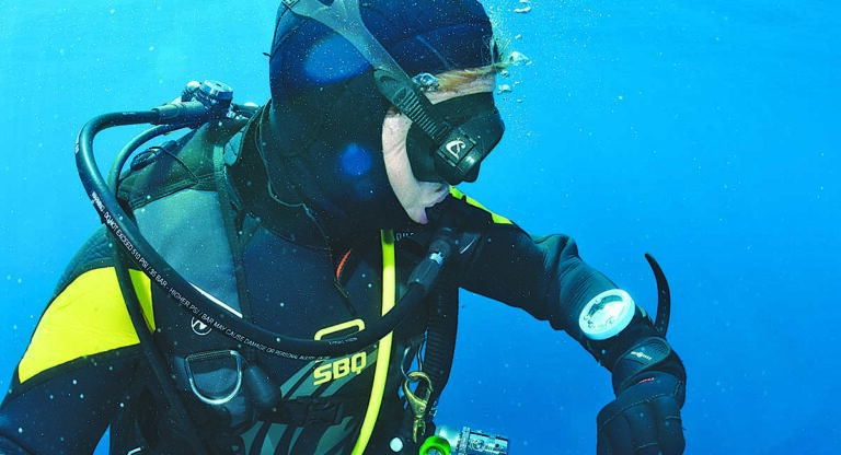 Plongée sous-marine avec un plongeur vérifiant son équipement dans un océan bleu cristallin.