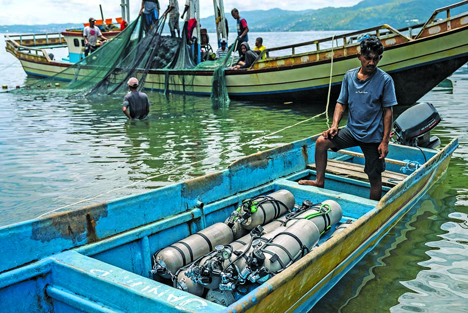 A diver prepares his equipment in a boat, surrounded by fishermen at sea.