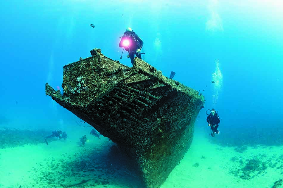 Two divers explore a shipwreck covered in corals, revealing the beauty of the underwater world.