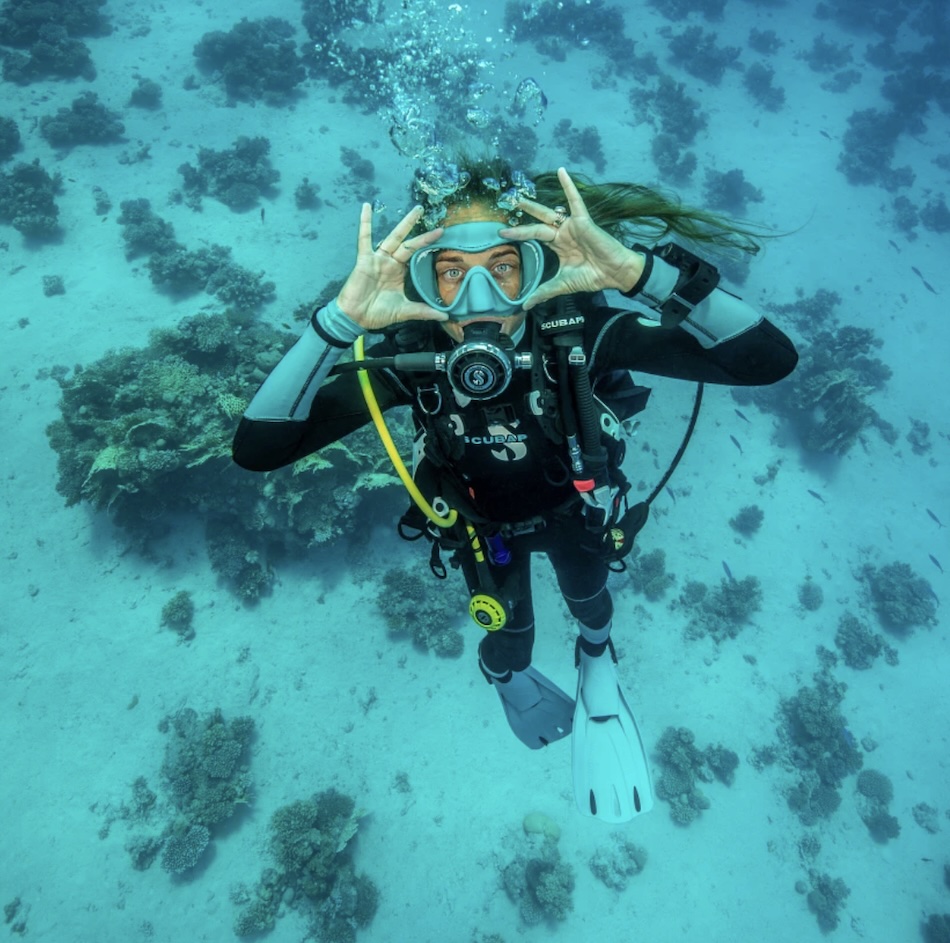 Smiling diver exploring the underwater world, surrounded by corals and colorful fish.