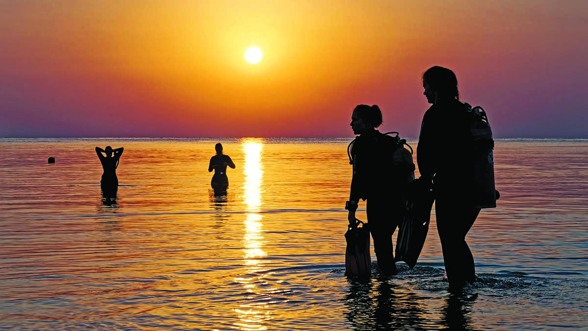 Des plongeurs émergent tranquillement des eaux, illuminés par un coucher de soleil spectaculaire.