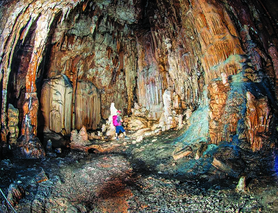 Un buceador explora una cueva submarina adornada con estalactitas y estalagmitas coloridas.