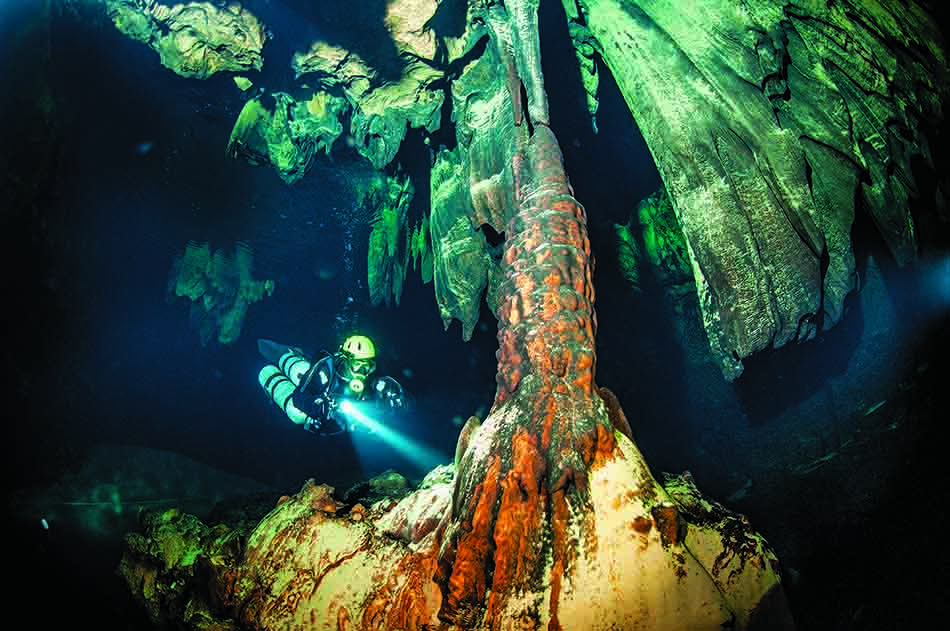 Un buceador explora una cueva submarina adornada con formaciones rocosas fascinantes y coloridas.
