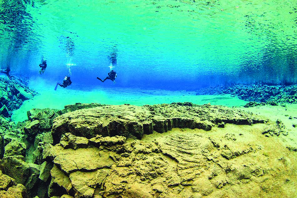 Buceadores exploran un paisaje submarino fascinante con formaciones rocosas y aguas cristalinas.